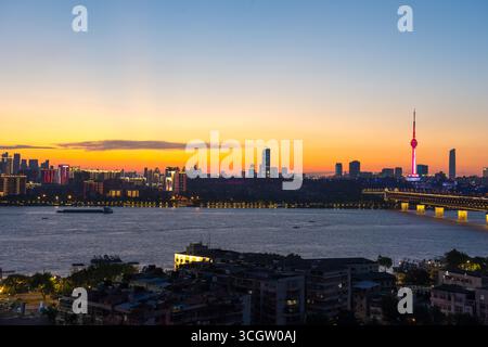 Lo skyline della città di Wuhan si illumina sul fiume Yangtze al tramonto, in Cina. Foto Stock