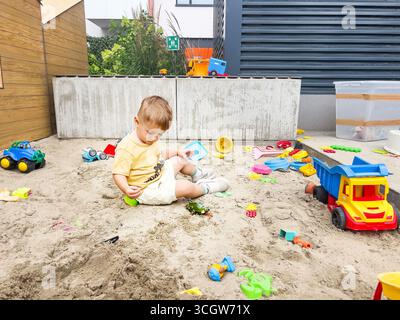 Bambini che giocano da soli in una scatola di sabbia con giocattoli in un parco giochi, godendo di attività all'aperto Foto Stock