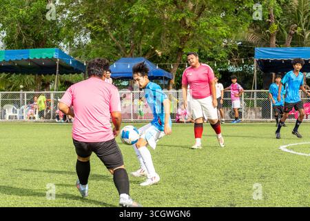 Una vista di due giocatori di calcio di diverse squadre che competono per il pallone all'ufficio distrettuale di Koh Chang nel villaggio di Dan mai sull'isola di Koh Chang. La comunità locale nel villaggio di Dan mai, sull'isola di Koh Chang, Thailandia, ha organizzato un torneo di calcio di beneficenza domenica 24 agosto 2025. I partecipanti includevano residenti locali, espatriati, visitatori e agenti di polizia della stazione di polizia locale, tutti insieme per raccogliere fondi per il Dan mai Hospital, un ospedale governativo pubblico. Questi eventi fanno parte di uno sforzo più ampio per sostenere l'ospedale nell'acquisizione di attrezzature aggiuntive e nel miglioramento della sua f Foto Stock