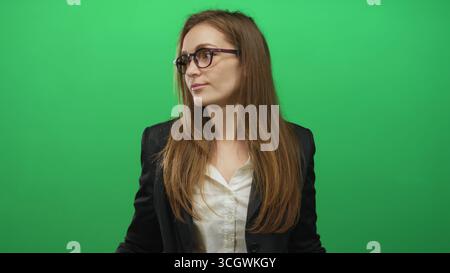 Una donna stringe le mani in uno studio verde mentre inclina la testa e chiude gli occhi con un leggero sorriso; incertezza dubbio confusione indecisione. Foto Stock