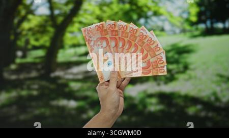 Uomo caucasico che tiene all'aperto diverse banconote in peso filippino in un parco, mettendo in evidenza un concetto di ricchezza o finanza in un ambiente naturale Foto Stock