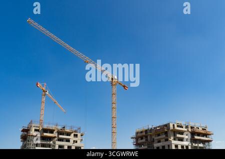 Due grandi gru industriali gialle che operano in un cantiere di case di appartamenti. Foto Stock