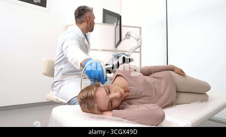 Il sonografo esamina il cervello della paziente ponendo il trasduttore a ultrasuoni sulla tempia della testa della paziente. Ecografia vascolare dell'emicrania Foto Stock