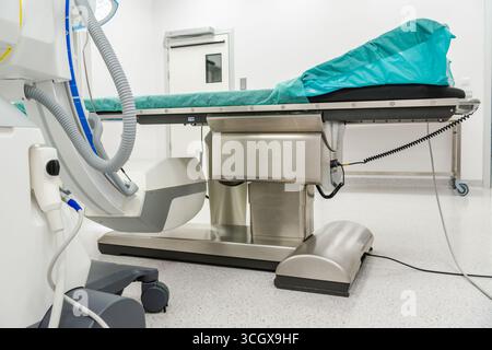 Una sala operatoria ospedaliera organizzata dispone di un tavolo d'esame pulito, apparecchiature mediche e illuminazione luminosa tipica di un ambiente chirurgico. Foto Stock