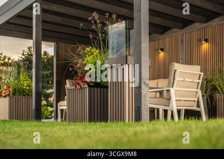 Un'accogliente area salotto all'aperto dispone di comode sedie e piante vivaci, ideale per rilassarsi in un giardino al tramonto. Foto Stock