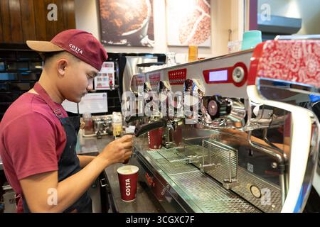 Langkawi, Malesia - 20 luglio 2024: Giovane barista maschile che prepara il caffè al Costa Coffee, aeroporto di Langkawi. Macchina per il caffè a fuoco. Foto Stock