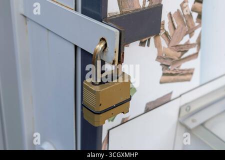 Uno scatto ravvicinato di un lucchetto in ottone resistente agli agenti atmosferici su una barra di sicurezza in metallo contro un muro rustico. Foto Stock