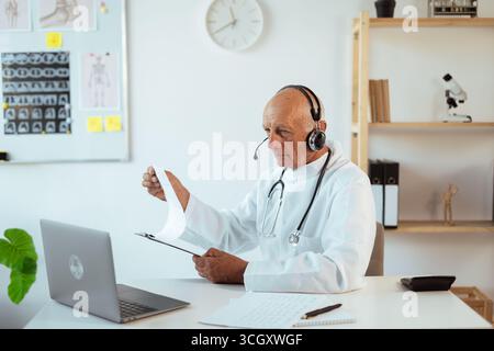 Medico anziano che lavora online consultando paziente nel concetto di telemedicina Foto Stock