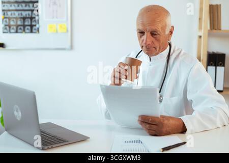 medico di sesso maschile che lavora con documenti che bevono caffè durante il turno in clinica, copia spazio Foto Stock