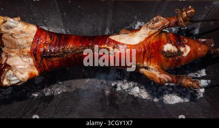 Un giovane maiale viene arrostito con uno sputo sopra i carboni. Foto Stock