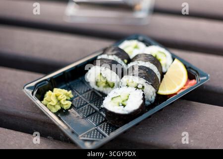 Gli involtini di sushi riempiti di cetriolo sono ordinatamente disposti su un vassoio nero Una bambole di wasabi e una fetta di limone completano i panini, creando un Foto Stock