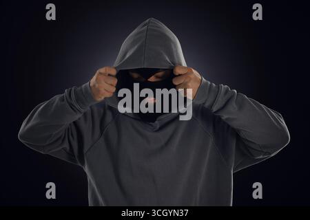 Criminale in maschera e cappuccio su sfondo scuro Foto Stock