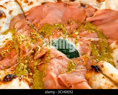Pizza appena sfornata con mortadella, pesto, pistacchio e basilico su un tavolo di legno. Cultura gastronomica, gastronomia e tradizione culinaria Foto Stock