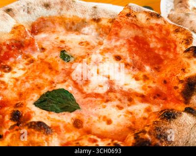Pizza appena sfornata con mortadella, pesto, pistacchio e basilico su un tavolo di legno. Cultura gastronomica, gastronomia e tradizione culinaria Foto Stock