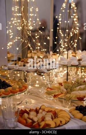 Lussuoso buffet di dessert caratterizzato da banchi di frutta a più livelli, pasticcini in miniatura e dolci delicati, delicatamente illuminati da scintillanti luci delle fate, creando un Foto Stock