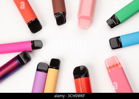 Varie penne monouso colorate disposte in cerchio su sfondo bianco, moderni dispositivi elettronici per fumatori. Foto Stock