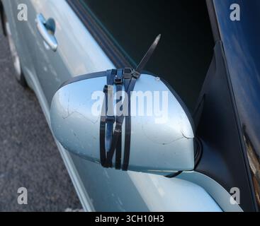 Primo piano di Uno specchietto laterale di Un'auto fissato con fascette serrafili dopo un danno, mostrando Una riparazione temporanea fai da te Foto Stock
