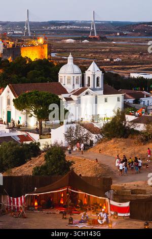 Castro Marim, Portogallo, 29 agosto 2025. La chiesa imbiancata di Castro Marim si erge sopra un vibrante campo medievale mentre la notte si avvicina, Algarve, Portug Foto Stock