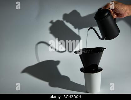 Una natura morta minimalista e artistica del processo di estrazione del caffè con effetto "pour-over", con una forte ombra grafica. Un concetto per caffè artigianale, precisione, AN Foto Stock