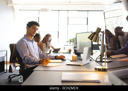 Professionisti diversi che collaborano alla scrivania, utilizzano laptop e prendono appunti Foto Stock