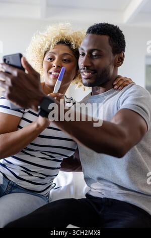 Coppia che celebra il risultato positivo del test di gravidanza mentre prende selfie a casa Foto Stock