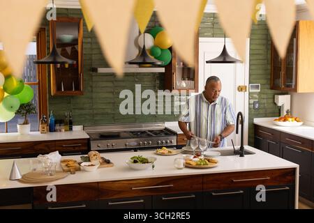 Uomo anziano che prepara insalata in cucina moderna con decorazioni natalizie Foto Stock