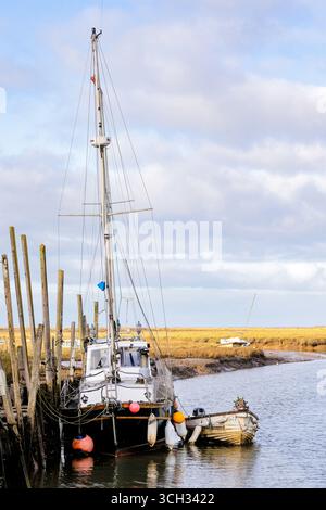 Una piccola barca riposa tranquillamente lungo un molo in legno lungo il fiume, che si riflette nelle acque calme sotto il verde delle sorgenti. Foto Stock