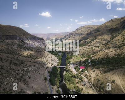 Vista aerea del fiume tortuoso che riflette il cielo luminoso tra le colline, un ponte che attraversa le acque, Vardzia, Samtskhe-Javakheti, Georgia. Foto Stock