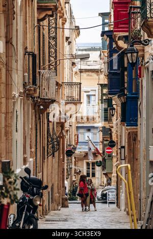 La Valletta, Malta - 10 aprile 2025: Ripida vista sulla strada con balconi tradizionali e bandiera maltese in riva al mare Foto Stock
