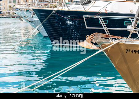Birgu, Malta - 11 aprile 2025: Vista ravvicinata di archi e ancore di yacht di lusso che si riflettono nelle acque turchesi del porto turistico di Birgu Foto Stock