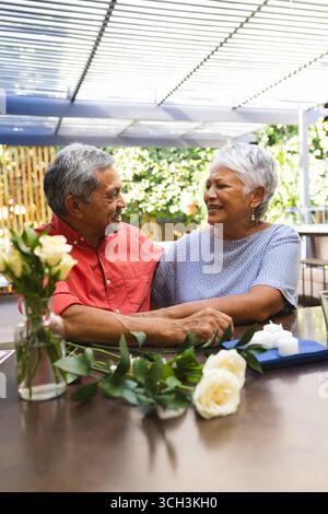 Coppie anziane sorridenti e diverse che si divertono insieme in un caffè in giardino con fiori Foto Stock