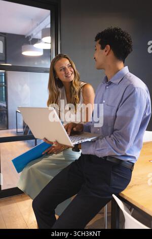Colleghi diversi che discutono di progetti mentre utilizzano un notebook in un ufficio moderno Foto Stock