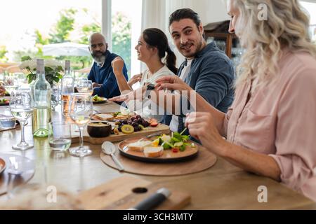 Amici che si godono una conversazione vivace e un pasto delizioso in un piccolo ricevimento di nozze informale, a casa Foto Stock