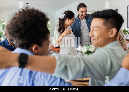 Ospiti che festeggiano insieme in un piccolo ricevimento di nozze informale, sorridendo e godendo momenti, a casa Foto Stock