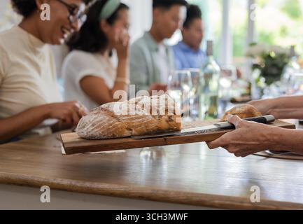 Amici che si godono il pane durante un piccolo ricevimento di nozze informale, condividono risate e conversazioni, a casa Foto Stock