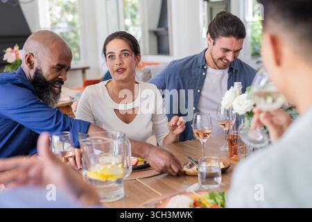 Amici che si divertono a ridere e chiacchierare durante il pranzo in occasione di una piccola cerimonia di nozze informale, a casa Foto Stock