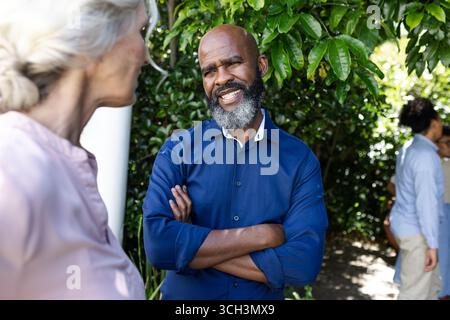 Uomo sorridente in camicia blu che chiacchiera con la donna durante un piccolo ricevimento di nozze informale all'aperto, a casa Foto Stock