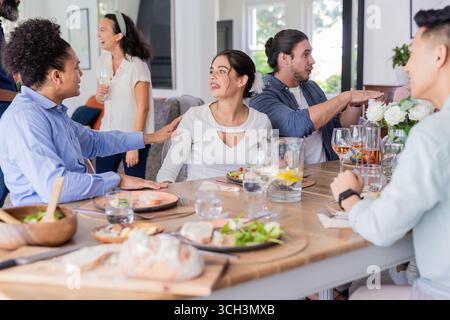 Amici che si godono una conversazione e un drink al tavolo elegante e informale per ricevimenti nuziali, a casa Foto Stock