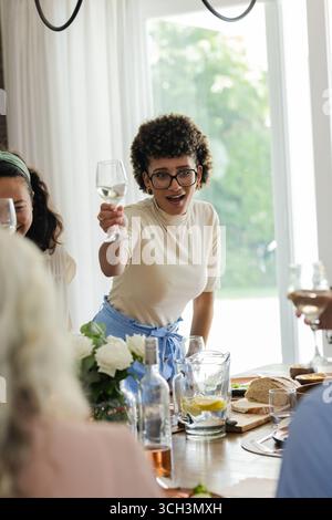 Durante un piccolo ricevimento di nozze informale, una donna che brinda un bicchiere, festeggia con gli amici, a casa Foto Stock
