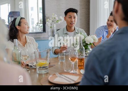 Amici che si godono una conversazione e un drink al tavolo elegante e informale per ricevimenti nuziali, a casa Foto Stock