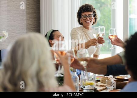 Brindate con bicchieri da vino, amici che celebrano un piccolo matrimonio informale e sorridono insieme, a casa Foto Stock