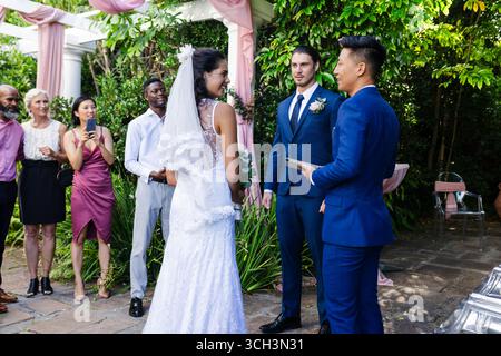 Sposa e sposo si scambiano le promesse all'aperto, circondati da amici e familiari gioiosi Foto Stock