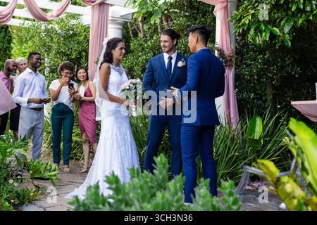 Sposa e sposo si scambiano le promesse all'aperto, circondati da amici e familiari gioiosi Foto Stock