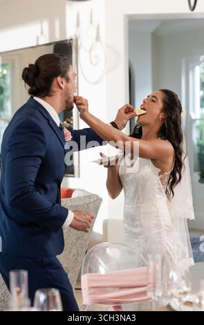 Sposa e sposo si nutrono gioiosamente a vicenda della torta al ricevimento di nozze Foto Stock