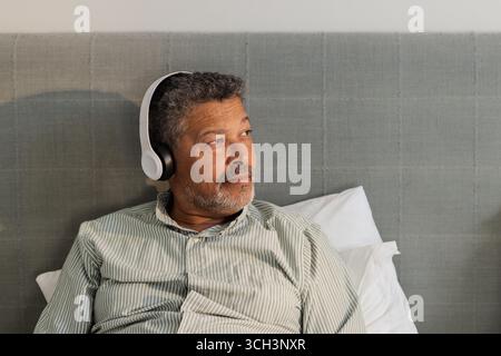 Rilassatevi a casa, un anziano che ascolta musica con le cuffie, con un aspetto accattivante Foto Stock