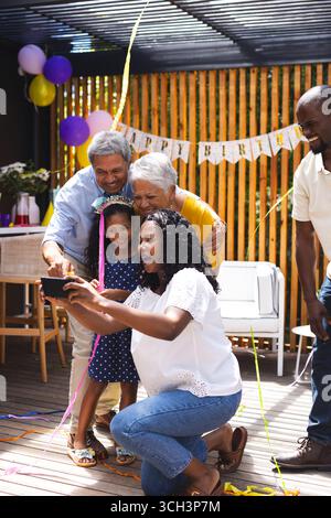 Alla festa, festeggiando il compleanno in giardino, la famiglia felice si fa selfie e decorazioni Foto Stock