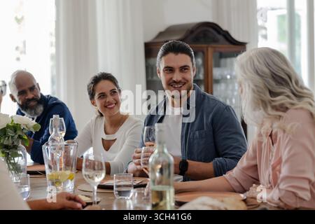 Amici che si godono una conversazione e un drink al tavolo elegante e informale per ricevimenti nuziali, a casa Foto Stock