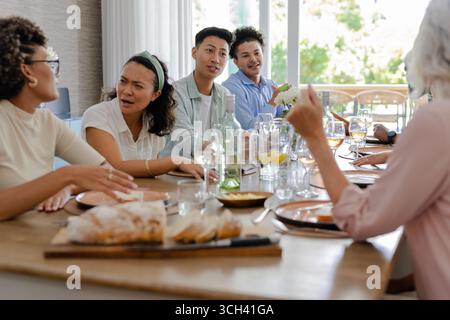 Al piccolo ricevimento di nozze informale, amici che condividono storie e risate intorno al tavolo, a casa Foto Stock