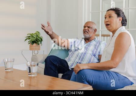 Guardare la televisione a casa, una coppia anziana seduta sul divano esprimendo una sorpresa Foto Stock