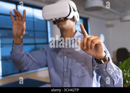 Uomo che utilizza un visore VR in ufficio e interagisce con un ambiente virtuale Foto Stock